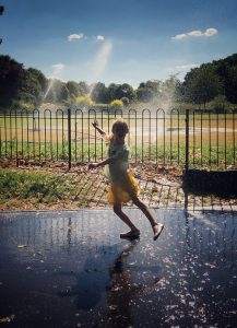 Vahe Saboonchian - daughter in Pitshanger Park with sprinklers behind on the bowling green