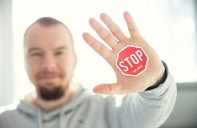 White man holding his hand up with STOP in red written on the hand