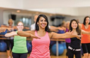 A woman is leading out in a fitness dance class at her indoor studio.