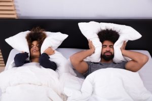 Couple laying in bed, covering their ears with their pillows