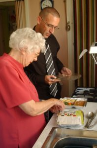Man helping elderly woman prepare her meal