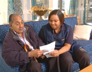 Black female carer helping older Asian man