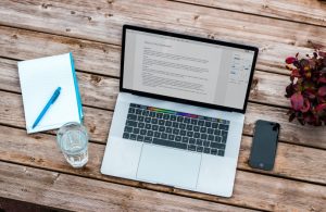 Laptop on a table with a glass of water, notebook and mobile phone