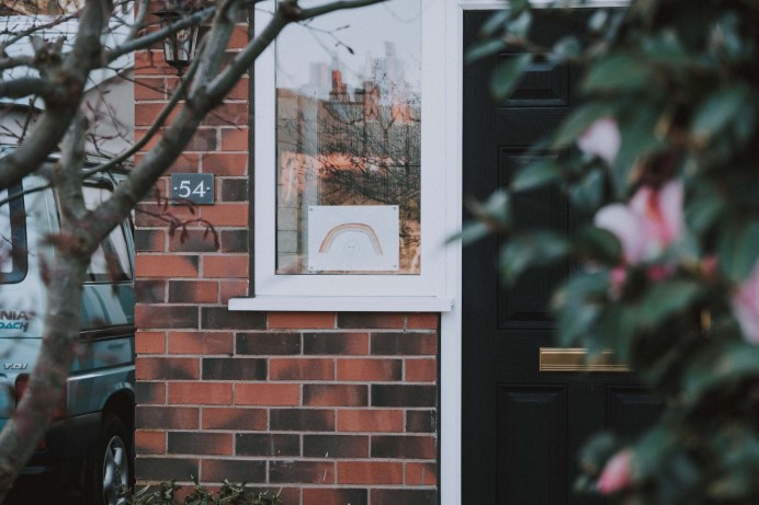 Front of a house with a black door and rainbow art in the window