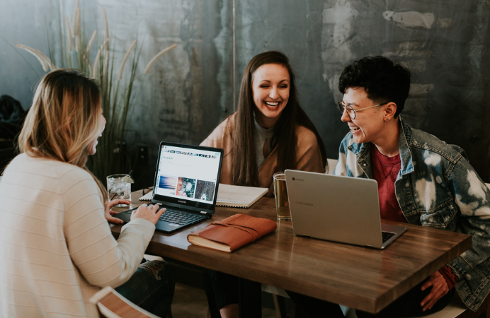 Three women in front of a desk with laptops laughing