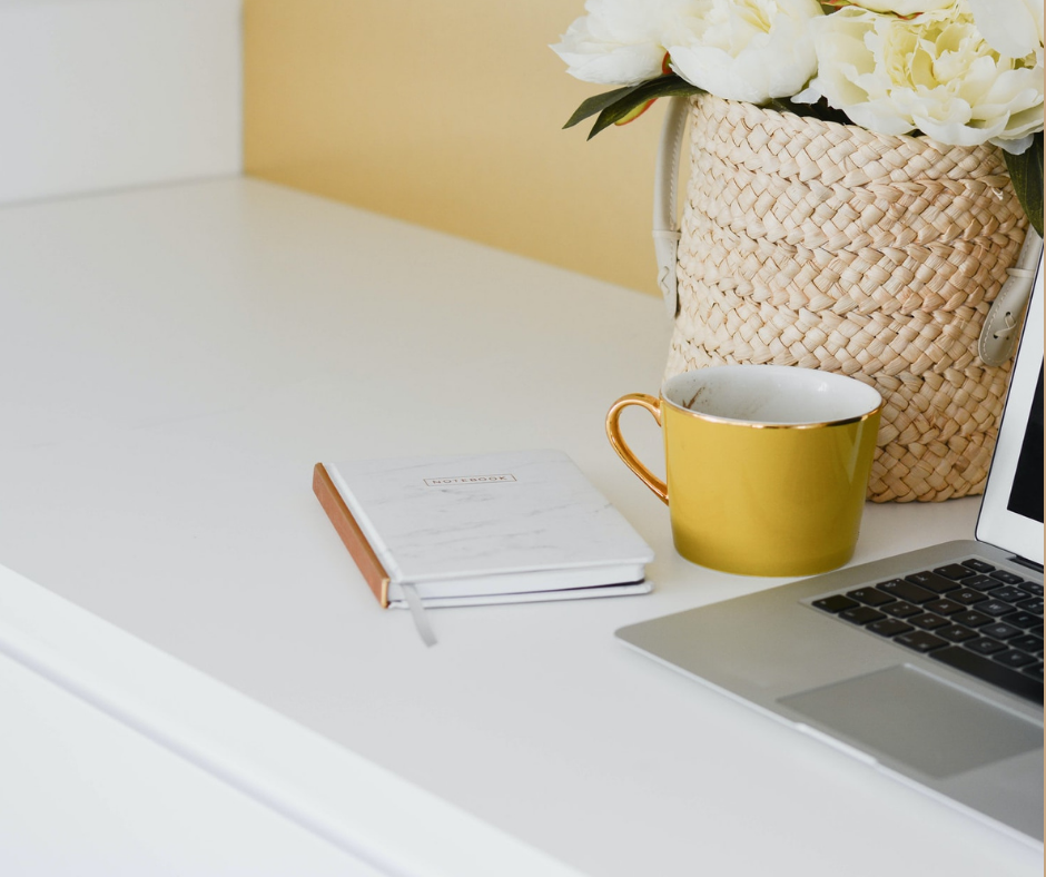 A desk with laptop, notebook and flowers