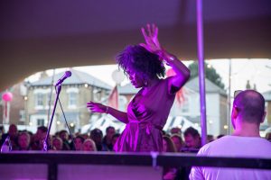 A singer dancing while performing at the Hanwell Hootie, with crowds behind looking on