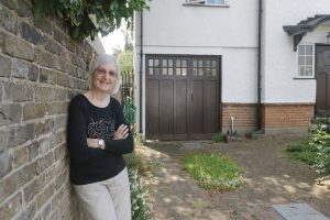 Woman standing in front of her driveway, which she has allowed to go 'green' with plants