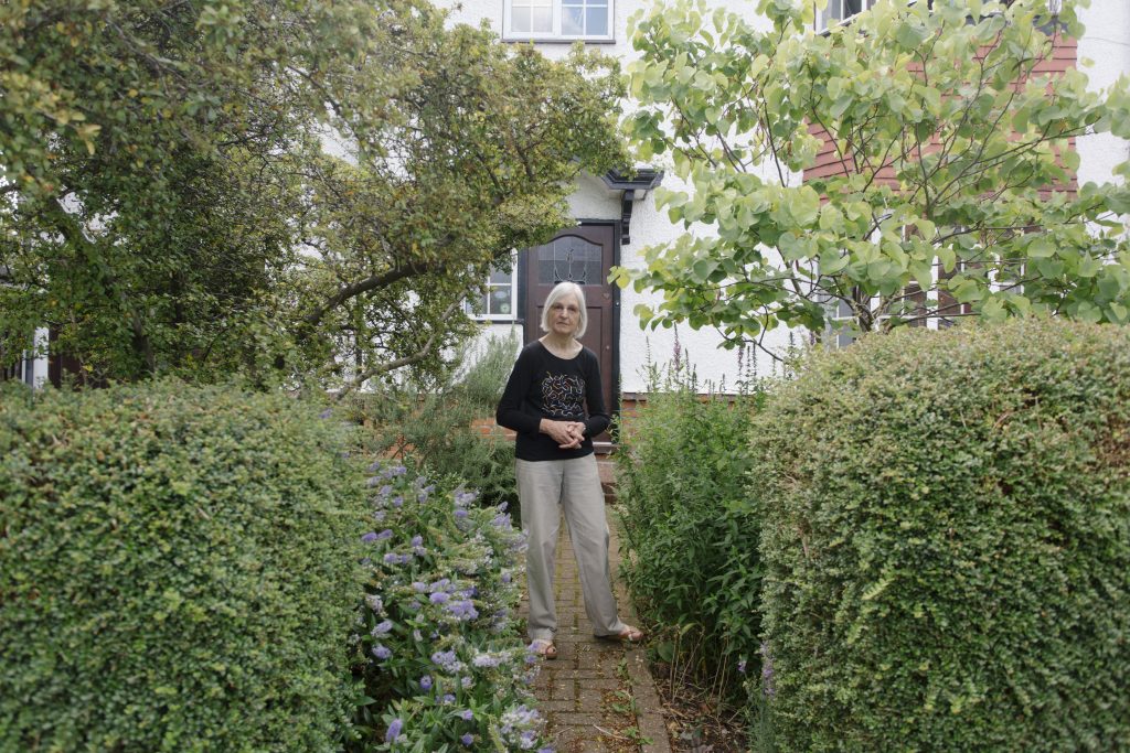 Woman standing in green front garden, surrounded by bushes and plants