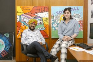 Man and woman sitting down in a room with colourful artwork on the wall behind them