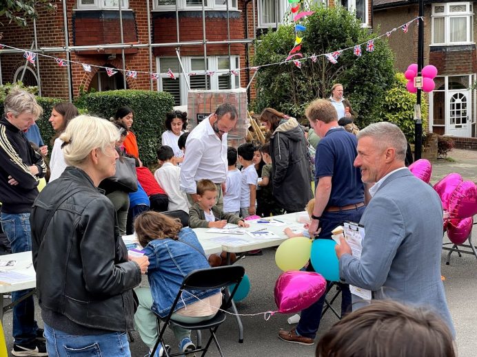 Adults watching children sitting at a table doing arts and crafts at a street party