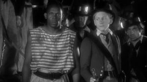 A man wearing an old striped sailor's uniform standing next to a ship's captain holding an old fashioned pistol - scene from 1935 movie Midshipman Easy