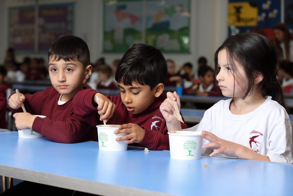 Three children eating food at a table at school