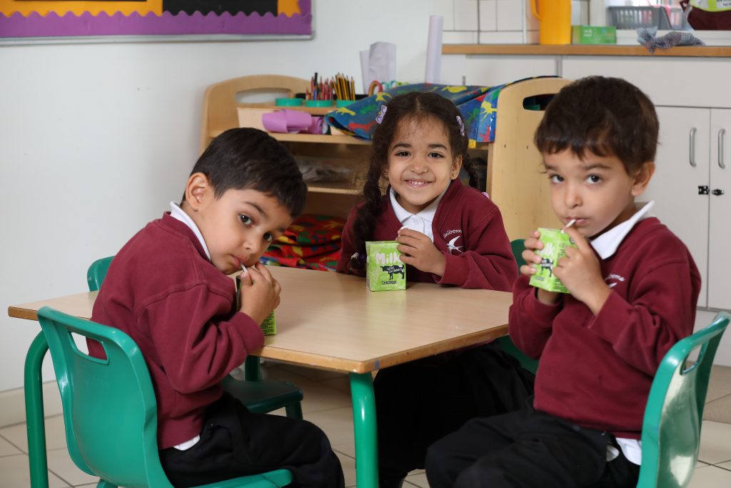 Three children at a desk at school having a drink