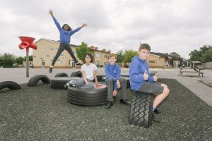 Grange Primary School pupils in the playground - one jumping in the air, one sitting with his thumbs up