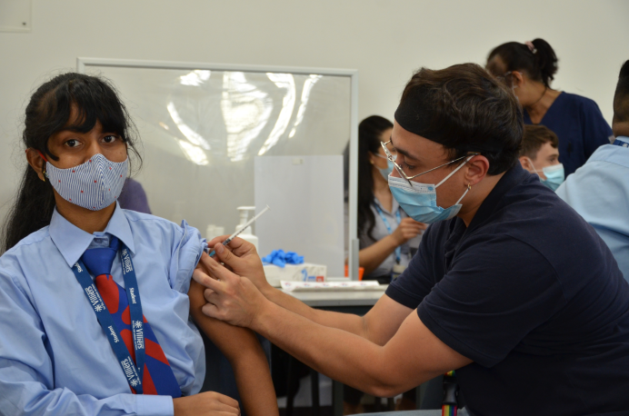 A schoolgirl being given a vaccine shot in the arm by a nurse
