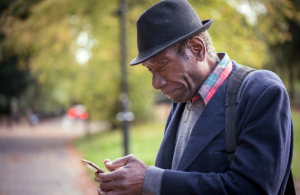 Older man sitting on a bench in park reading a phone
