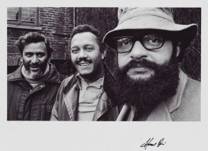 Three men looking at the camera. They are writers Samuel Selvon, John La Rose, and Andrew Salkey. It was taken by photographer Horace Ové