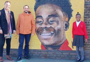 Cllr Peter Mason, Darek Urlewicz and Myla Clarke-Williams in front of painting of Bukayo Saka