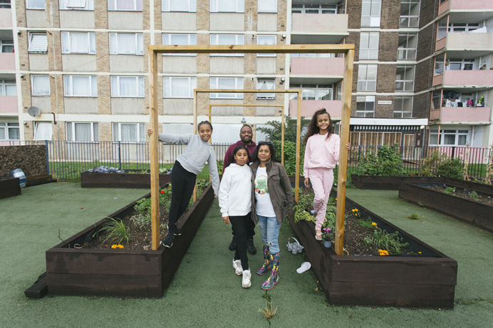 A man and woman with their two daughters and their friend, also a girl, standing in a community garden