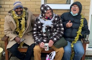 Three men sitting on a bench laughing with tinsel around their necks