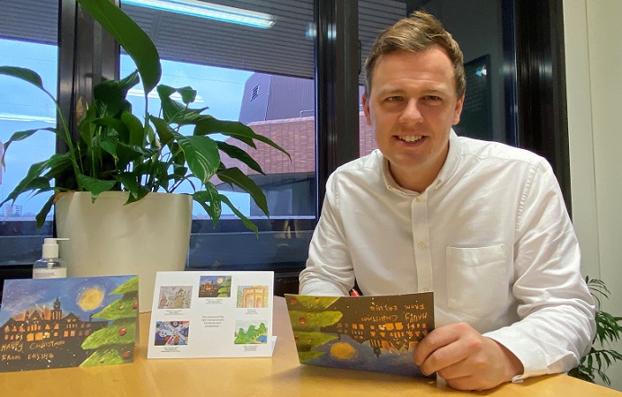 Councillor Peter Mason sitting at a desk with copies of the winning Christmas card entries and desk plant in plant pot