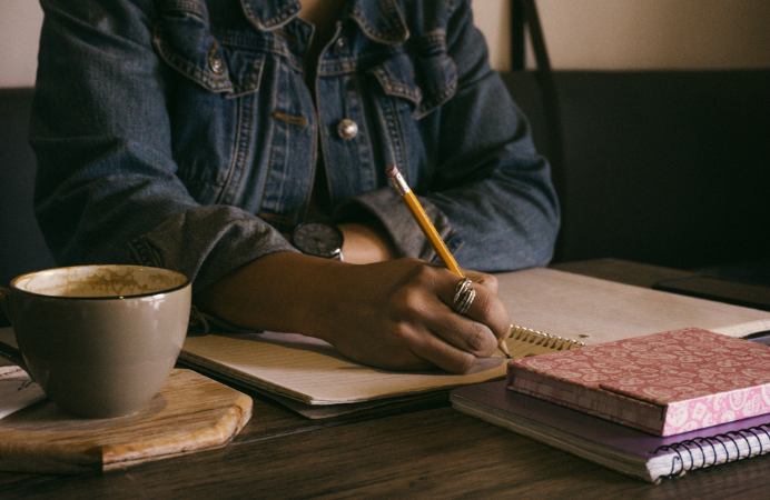 A black woman writing in a notepad with a cup of coffee