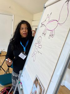 Woman holding pen next to big flipboard, with drawings on paper