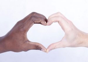 Two hands, one black and white, coming together to form a heart shape