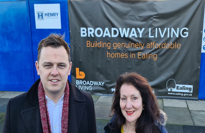 Man and a woman standing in front of a hoarding at a building site