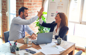 A male and female at an office desk giving each other high five