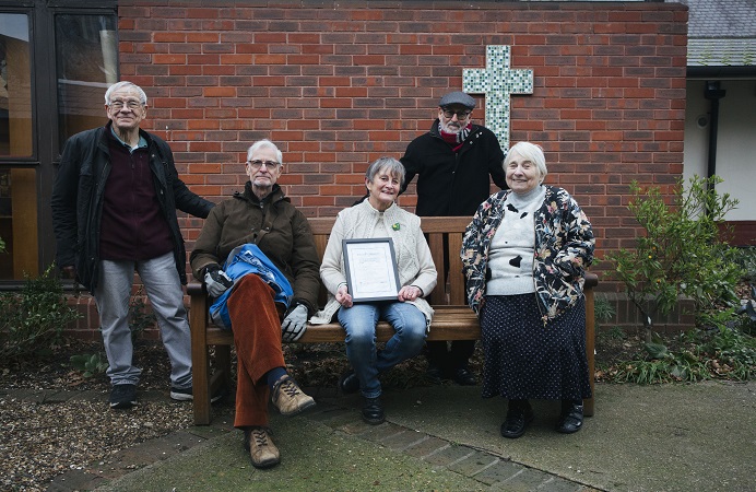 Members of a church pose outside on a bench with a certificate