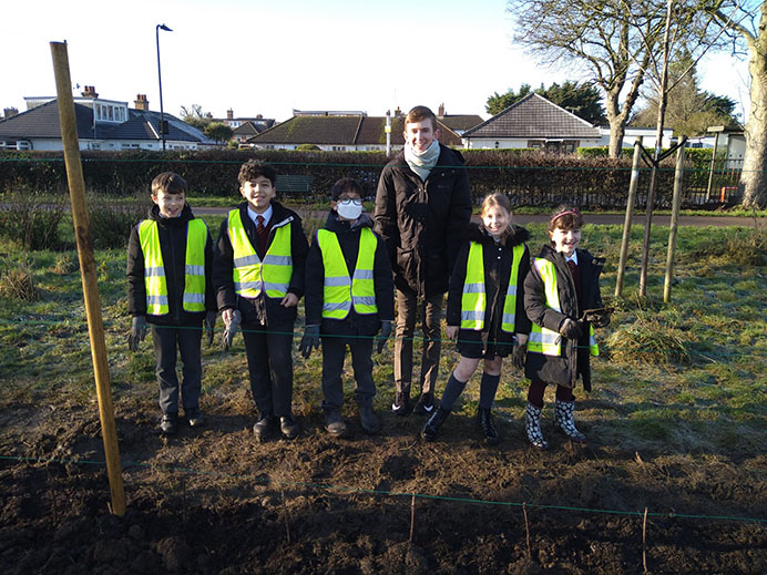 Five school children and a teacher standing on a playing field looking happy