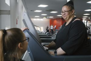Woman on a treadmill with personal trainer looking on