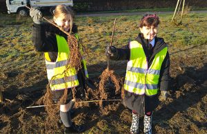 Two girls from local primary schools holding saplings up in the air before planting them