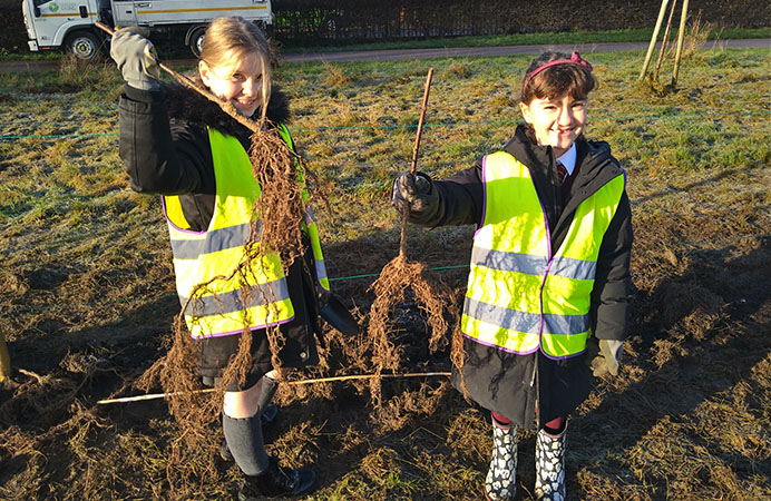 Two girls from local primary schools holding saplings up in the air before planting them