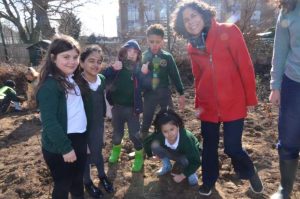 A group of school children standing with a woman next to a tree sapling they have planted