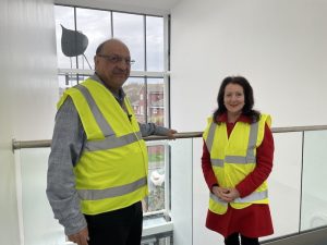 Councillors Manro and Wall standing in front of a balustrade wearing high-viz jackets at Poplars temporary housing unit