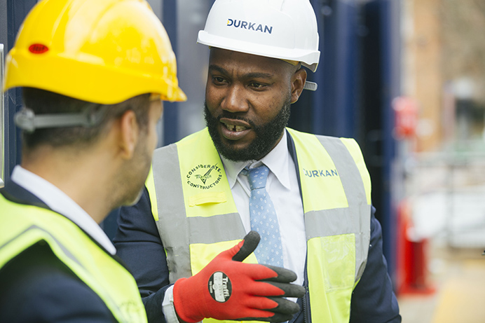 Two men talking on a building site, wearing safety clothing