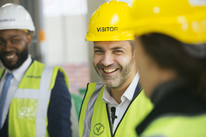 Three people on a building site, smiling and talking, wearing protective clothing