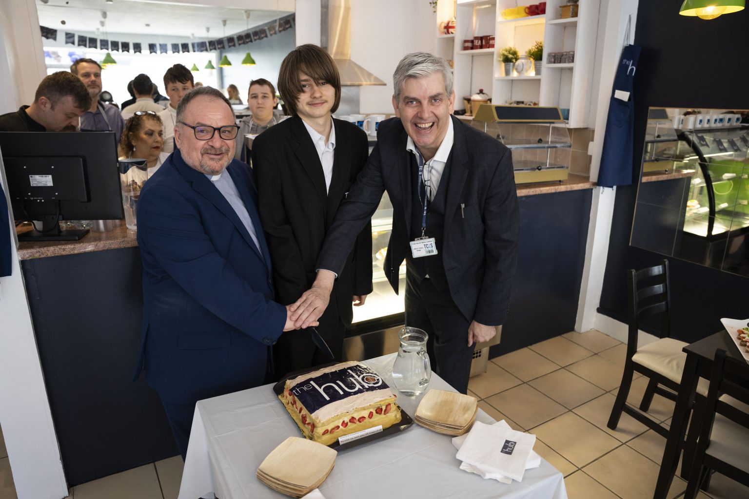 Two men and a teenager standing in front of a cake in a cafe