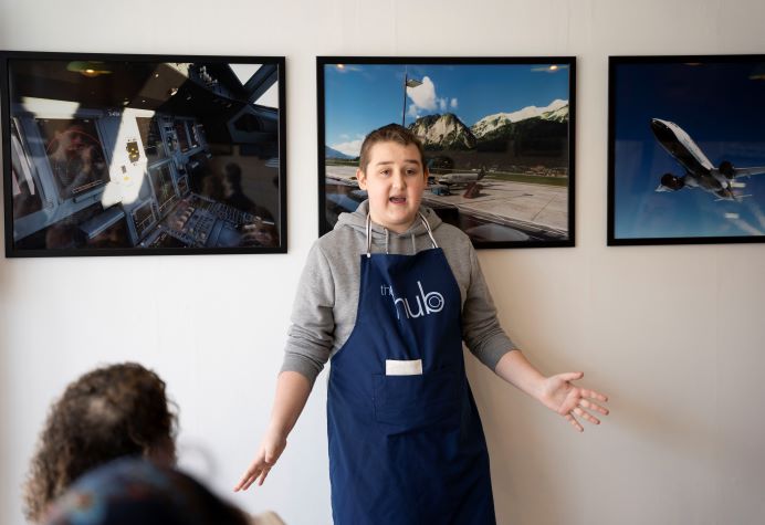 A teenager wearing an blue apron saying The Hub talking animatedly