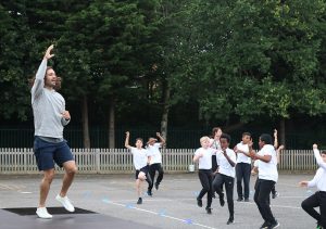 Man leading a work out on a school playground, with children joining in