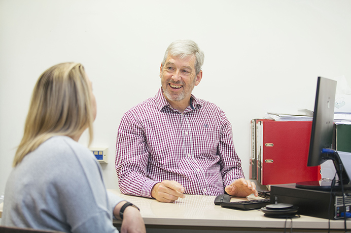 Smiling man behind desk talking to woman in front of desk