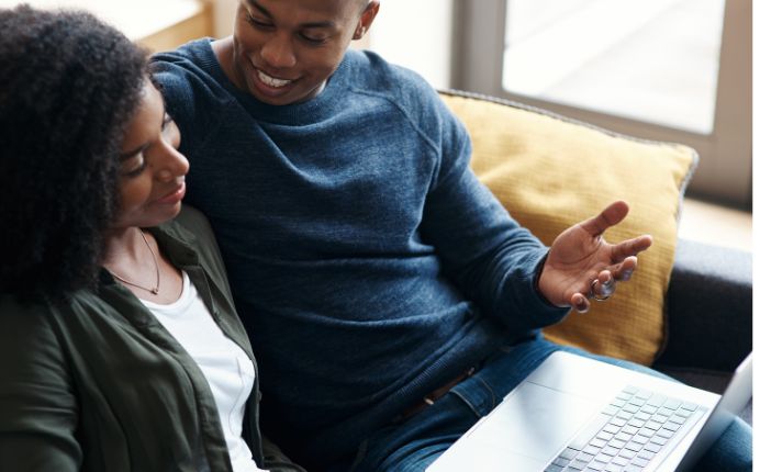 Black man and woman talk to each other in front of a laptop screen