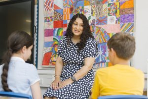 A woman talking to two school children in a classroom