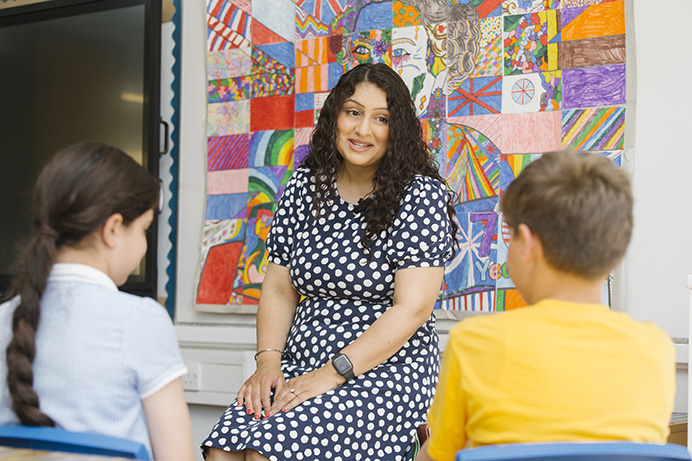 A woman talking to two school children in a classroom