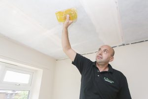 Man reaching up to scrape a ceiling