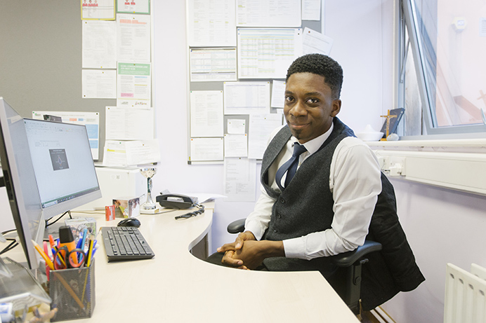 Man sitting at an office desk with a computer and looking at the camera