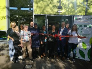 Group of smiling people outside Northolt library, cutting a red ribbon